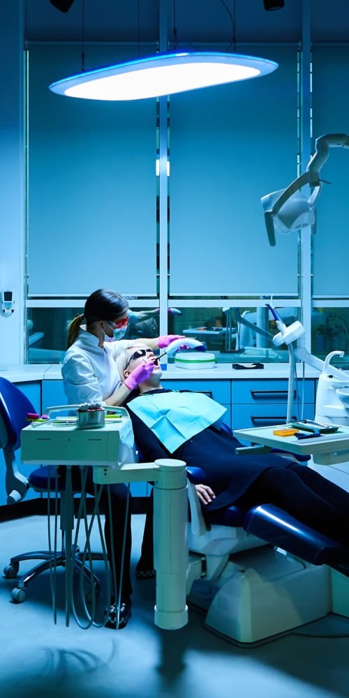 Female dentist examining and treating patient teeth in dental clinic